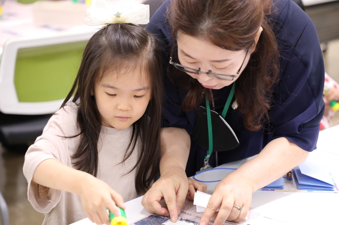강사가 다문화 가족 아이에게 ‘한지 북아트’ 만들기를 도와주고 있다.