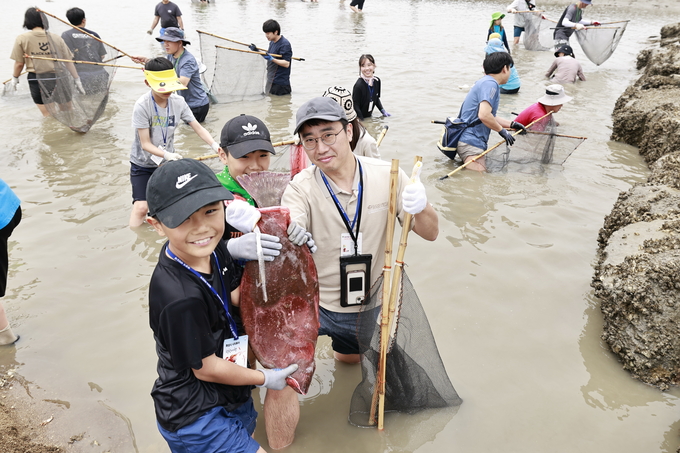 화성 뱃놀이 축제의 ‘독살 체험’ 프로그램에 참여한 가족이 직접 잡은 물고기를 들고 환하게 웃고 있다